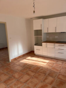 Cuisine moderne vide et lumineuse avec meubles blancs, plan de travail bois et carrelage terracotta. Espace rénové.