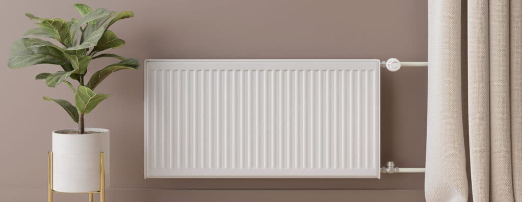 Radiateur blanc moderne, plante verte en pot blanc sur support doré, mur beige, rideaux beige à droite.
